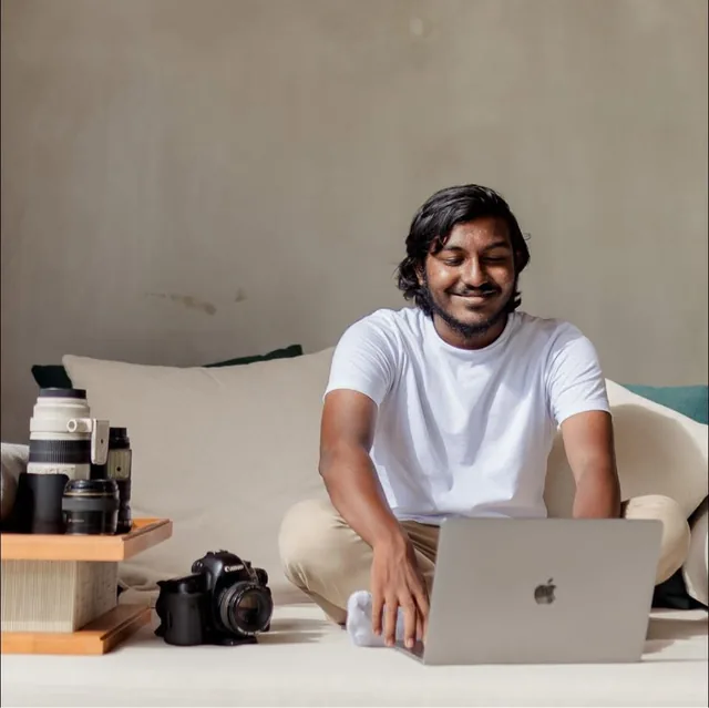 Ibrahim Ifaaz editing on a laptop, camera bodies and lenses beside him
