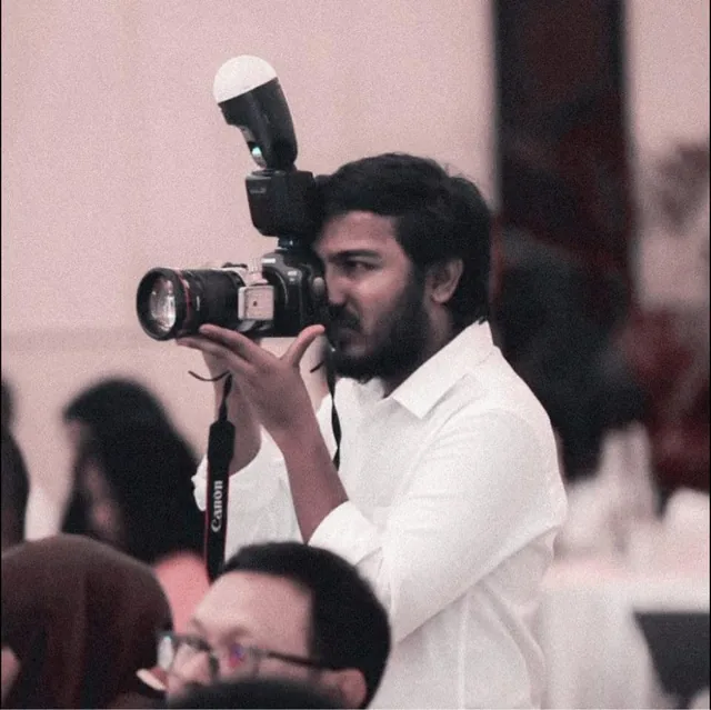 Ibrahim Ifaaz photographing an event, camera and flash raised to his eye